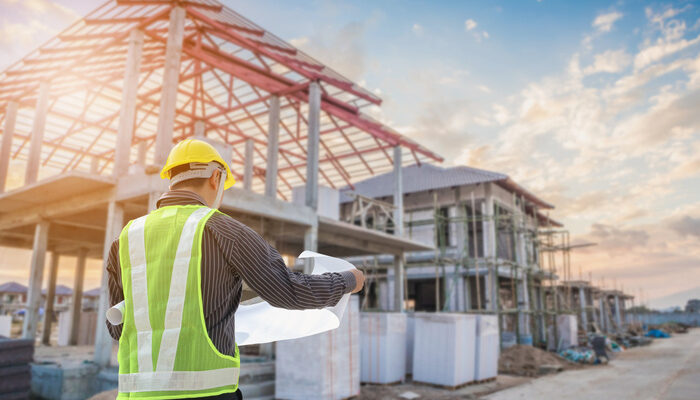custom home builder with protective helmet and blueprints paper at house building construction site background